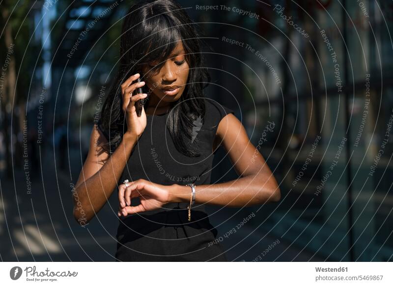 Geschäftsfrau, die ein Smartphone benutzt und die Uhrzeit in der Stadt abfragt Leute Menschen People Person Personen Afrikanisch Afrikanische Abstammung