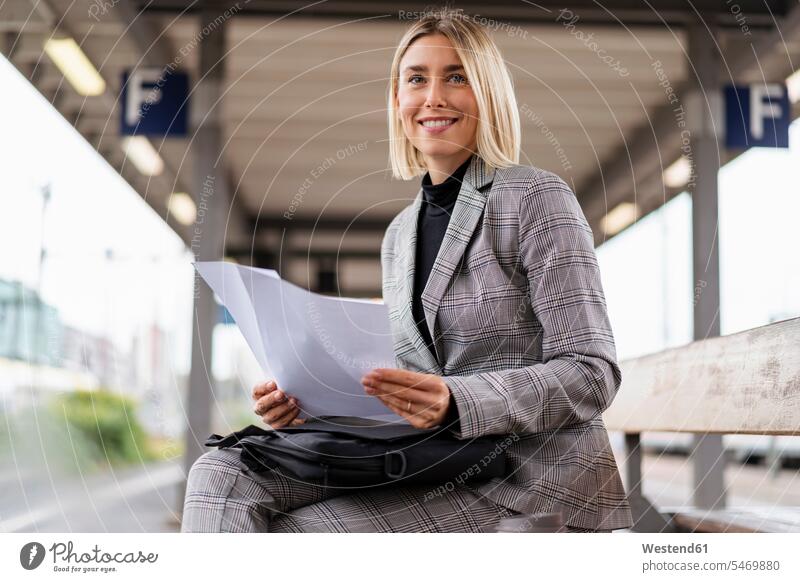 Lächelnde junge Geschäftsfrau mit Papieren am Bahnhof Job Berufe Berufstätigkeit Beschäftigung Jobs geschäftlich Geschäftsleben Geschäftswelt Geschäftsperson