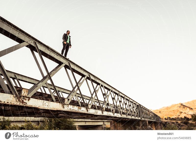 Mann steht auf der Metallstange einer alten Eisenbahnbrücke stehend alter altes frei Muße Individuell Lifestyles Courage mutig Tapferkeit riskant Wagnis