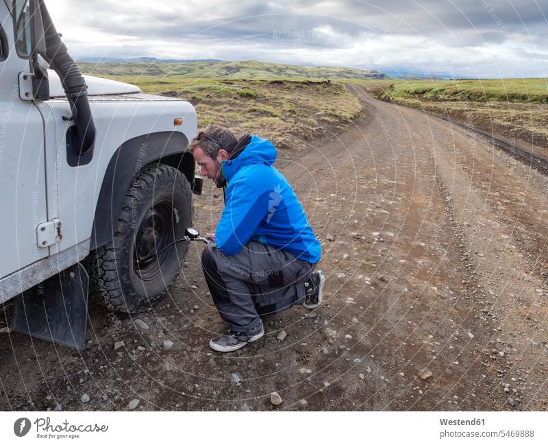 Mann kniend beim Prüfen des Reifendrucks durch Geräte am Straßenrand Farbaufnahme Farbe Farbfoto Farbphoto Island Republik Island Außenaufnahme außen draußen