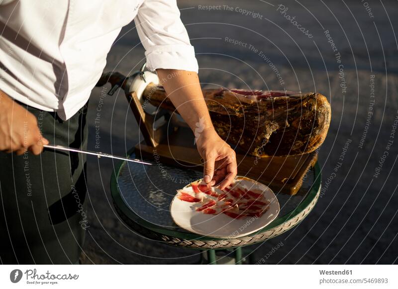 Männlicher Koch schneidet Schinkenscheiben auf dem Tisch, während er im Freien steht Farbaufnahme Farbe Farbfoto Farbphoto Spanien Tag Tageslichtaufnahme