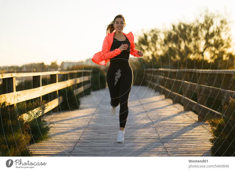 Lächelnde junge Frau läuft auf Fußgängerbrücke gegen klaren Himmel während Sonnenuntergang Farbaufnahme Farbe Farbfoto Farbphoto Spanien Sportkleidung