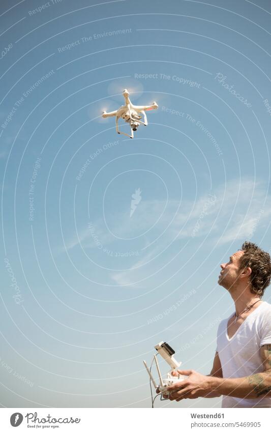 Mann fliegt Drohne unter blauem Himmel Drohnen fliegen fliegend Männer männlich Erwachsener erwachsen Mensch Menschen Leute People Personen Blick nach oben