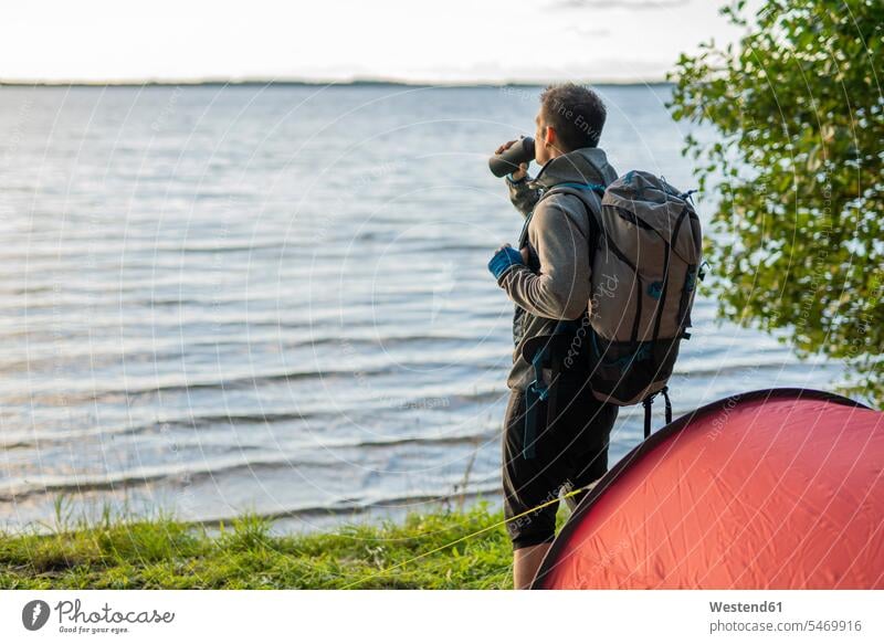 Mann zeltet in Estland, steht am See mit einem Rucksack, trinkt Kaffee Camping Campen zelten Zelt Zelte Wanderer Trinkflasche trinken Natur stehen stehend Seen