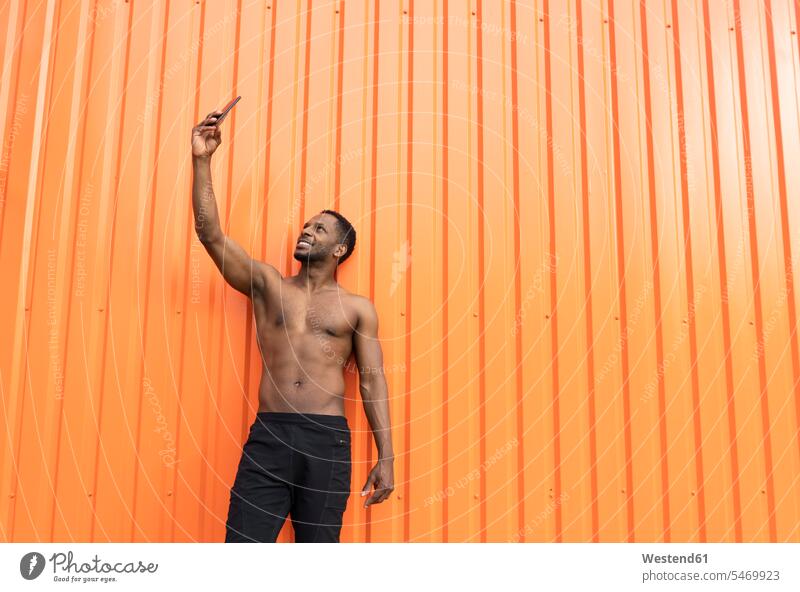 Porträt eines Sportlers, der ein Selfie vor einer orangefarbenen Wand macht Selbstportrait Selfies sich selbst fotografieren Selbstdarstellung Profilierung