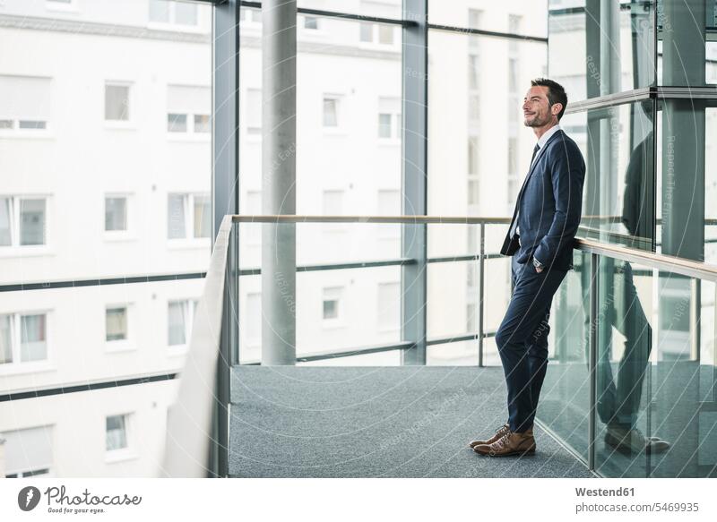 Erfolgreicher Geschäftsmann steht im Bürogebäude, schaut aus dem Fenster, träumt Office Büros Anzug Anzuege Anzüge stehen stehend anlehnen angelehnt lehnend