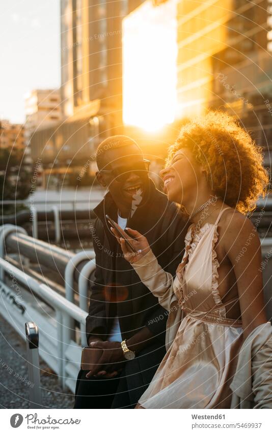 Glückliches Paar mit Handys in der Stadt bei Sonnenuntergang staedtisch städtisch Sonnenuntergänge Mobiltelefon Handies Mobiltelefone Pärchen Paare