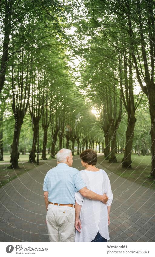 Rückansicht eines älteren Paares, das bei Sonnenuntergang in einem Park spazieren geht Partner Partnerschaften abends gefühlvoll Emotionen Empfindung