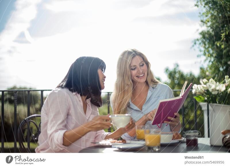 Zwei Frauen frühstücken an einem Café-Tisch im Freien und lesen ein Buch Leute Menschen People Person Personen Asiaten Asiatisch asiatische