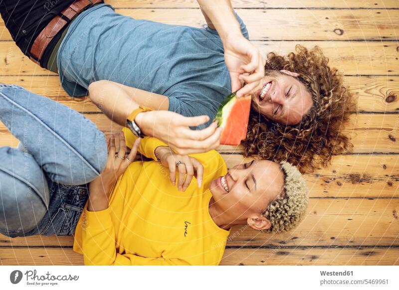 Glückliches junges Paar liegt zu Hause auf dem Boden und teilt sich eine Wassermelone Hochschueler Hochschüler Studenten Studierende Studierender entspannen