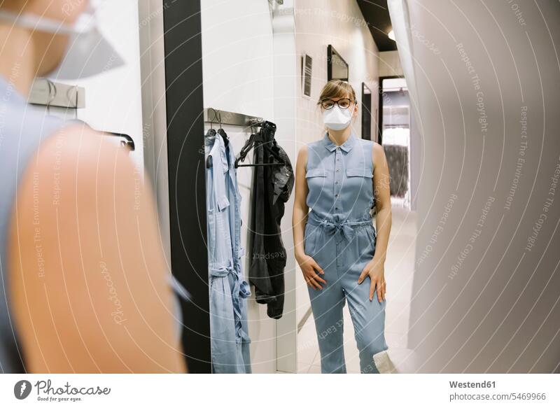 Frau mit Gesichtsmaske beim Anprobieren von Kleidung in einem Modegeschäft Brillen sich anziehen Kauf Einkauf Einkaufen shoppen shopping umziehen Gesundheit