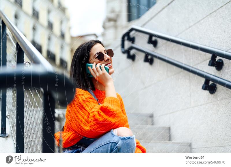 Lächelnde Frau, die auf der Treppe sitzend per Handy telefoniert Farbaufnahme Farbe Farbfoto Farbphoto Außenaufnahme außen draußen im Freien Tag