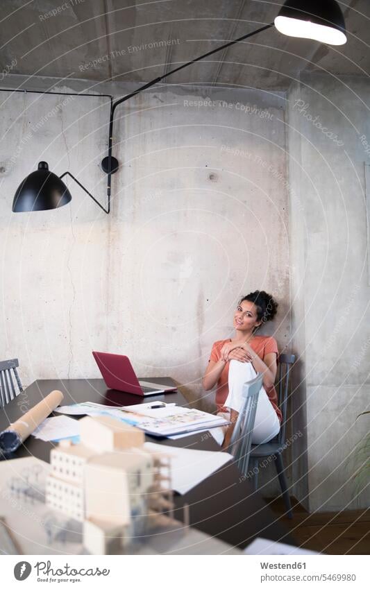 Porträt der lächelnden Geschäftsfrau sitzt am Tisch in einem Loft mit Dokumenten und Laptop Lofts Unterlagen Notebook Laptops Notebooks Geschäftsfrauen