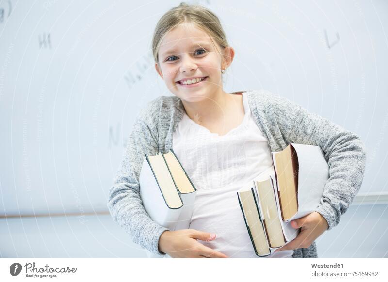 Porträt eines glücklichen Schulmädchens, das Bücher in der Klasse trägt Buch Schülerin Schuelerin Schülerinnen Schuelerinnen Portrait Porträts Portraits