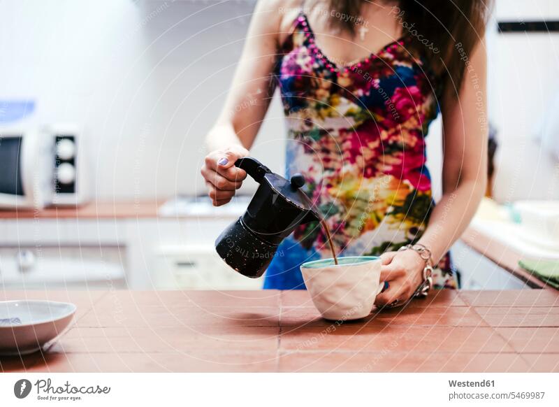 Frau gießt Kaffee in Kaffeetasse ein, während sie zu Hause in der Küche steht Farbaufnahme Farbe Farbfoto Farbphoto Innenaufnahme Innenaufnahmen innen drinnen