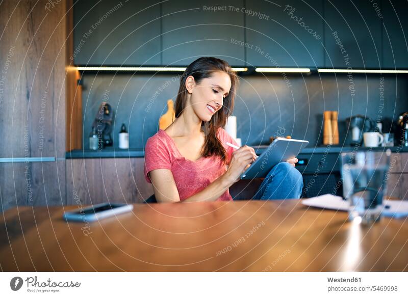 Lächelnde Unternehmerin benutzt digitales Tablet, während sie am Schreibtisch im Heimbüro sitzt Farbaufnahme Farbe Farbfoto Farbphoto Freizeitkleidung