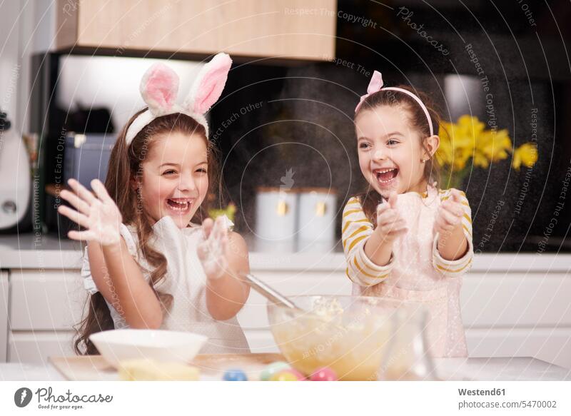 Zwei verspielte Schwestern haben Spaß beim gemeinsamen Backen von Osterkeksen in der Küche Spass Späße spassig Spässe spaßig Ostern Osterfest spielerisch backen