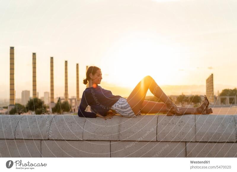 Spanien, Barcelona, Montjuic, junge Frau liegend auf einer Mauer bei Sonnenuntergang Mauern Sonnenuntergänge weiblich Frauen liegt Stimmung stimmungsvoll