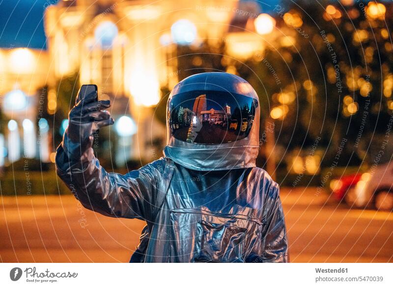 Spaceman auf einer Straße in der Stadt in der Nacht hält Smartphone Raumfahrer Weltraumfahrer halten nachts Handy Mobiltelefon Handies Handys Mobiltelefone