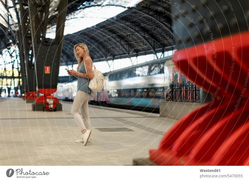 Junge Frau mit Handy auf dem Bahnhof Bahnhöfe Bahnhoefe Mobiltelefon Handies Handys Mobiltelefone weiblich Frauen Station Haltestelle Haltestellen Stationen