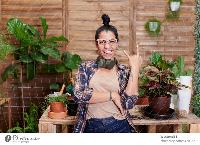 Porträt einer glücklichen jungen Frau, die auf ihrer Terrasse gärtnert Blumentoepfe Blumentöpfe Tische Holztische Kopfhoerer Brillen entspannen relaxen