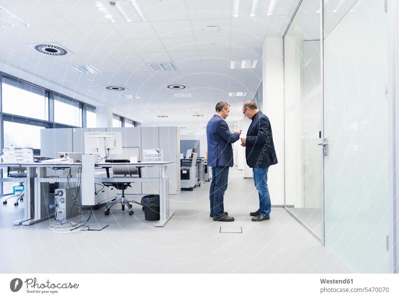 Zwei Geschäftsleute stehen im Büro und schauen auf ein Smartphone Arbeitskollege Arbeitskollegen Kollege Job Berufe Berufstätigkeit Beschäftigung Jobs