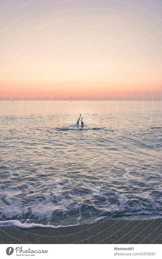 Teenager-Mädchen schwimmt bei Sonnenaufgang im Meer mit den Füßen gegen den Himmel Farbaufnahme Farbe Farbfoto Farbphoto Außenaufnahme außen draußen im Freien
