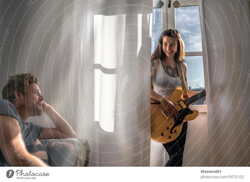 Mann schaut junge Frau zu Hause am Fenster mit einer Gitarre an Leute Menschen People Person Personen Europäisch Kaukasier kaukasisch gemischtrassig 2
