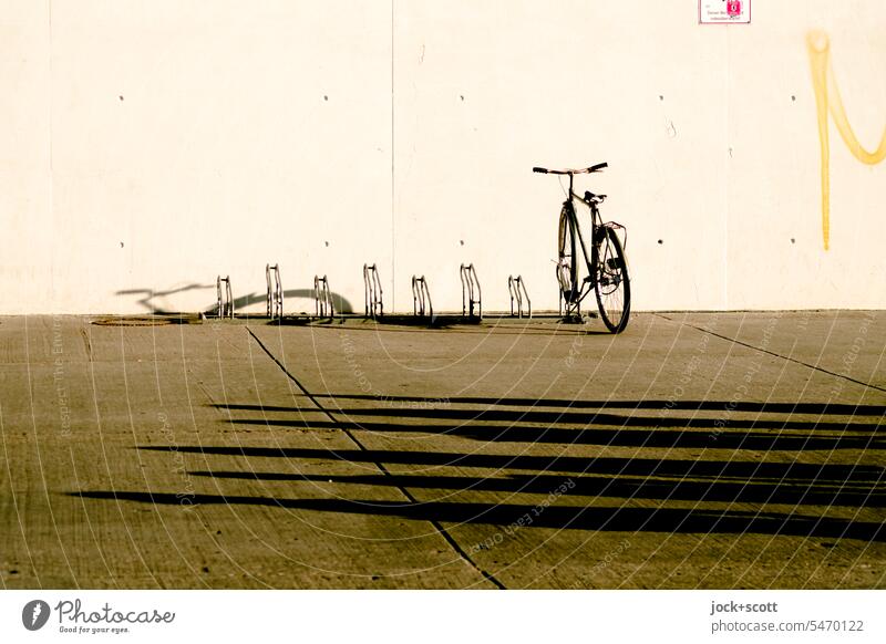 ein Fahrrad und lange Schatten auf dem Beton Fahrradständer parken Verkehrsmittel umweltfreundlich Betonwand Betonboden Parkplatz Schattenwurf abgestellt