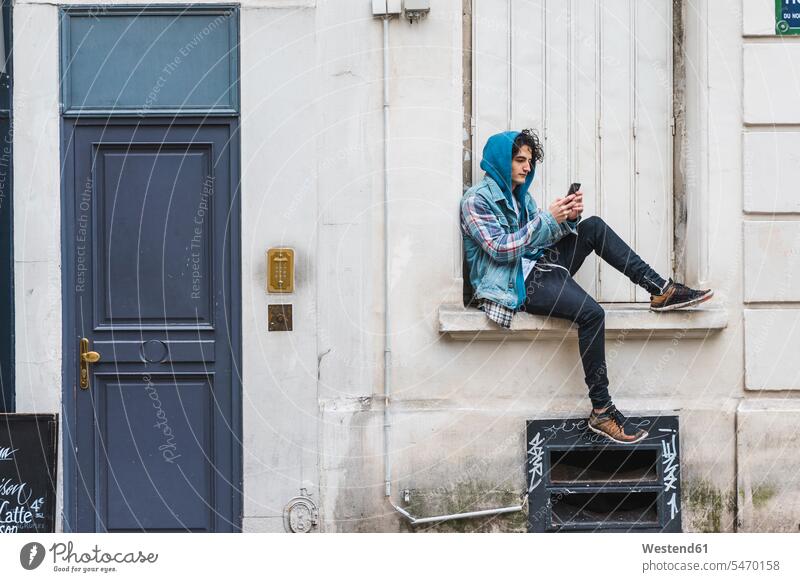 Junger Mann mit Smartphone auf dem Fensterbrett sitzend Männer männlich Individualität Individuell Handy Mobiltelefon Handies Handys Mobiltelefone iPhone