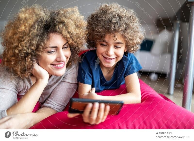 Mutter und Sohn sehen sich ein Video auf einem Smartphone an und liegen auf einem großen Kissen Leute Menschen People Person Personen Europäisch Kaukasier