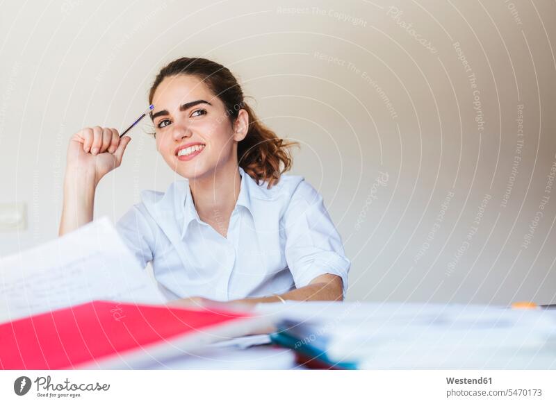 Lächelnde Studentin beim Lernen am Schreibtisch zu Hause Europäer eine Person junge Frau 25-30 Jahre Zufriedenheit lächeln vorbereiten smart Prüfung sitzen