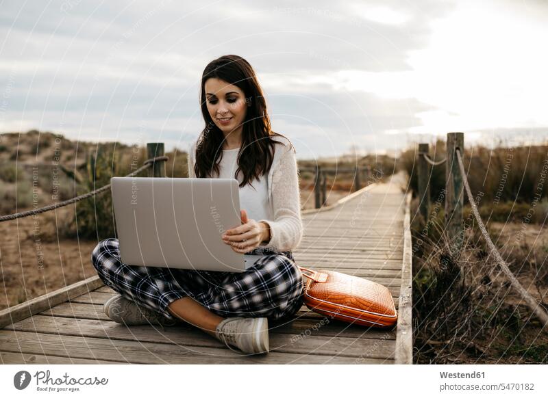Frau sitzt mit Laptop auf einer Promenade auf dem Land Taschen Rechner Laptops Notebook Notebooks Arbeit sitzend allein freuen zufrieden auf dem Lande Muße
