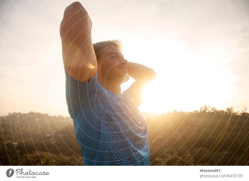 Mann streckt die Arme aus, während er gegen den Himmel steht Farbaufnahme Farbe Farbfoto Farbphoto Außenaufnahme außen draußen im Freien Sonnenuntergang