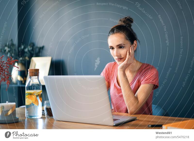 Unternehmerin mit Laptop auf dem Schreibtisch an der Wand im Heimbüro Farbaufnahme Farbe Farbfoto Farbphoto Freizeitkleidung Freizeitbekleidung casual
