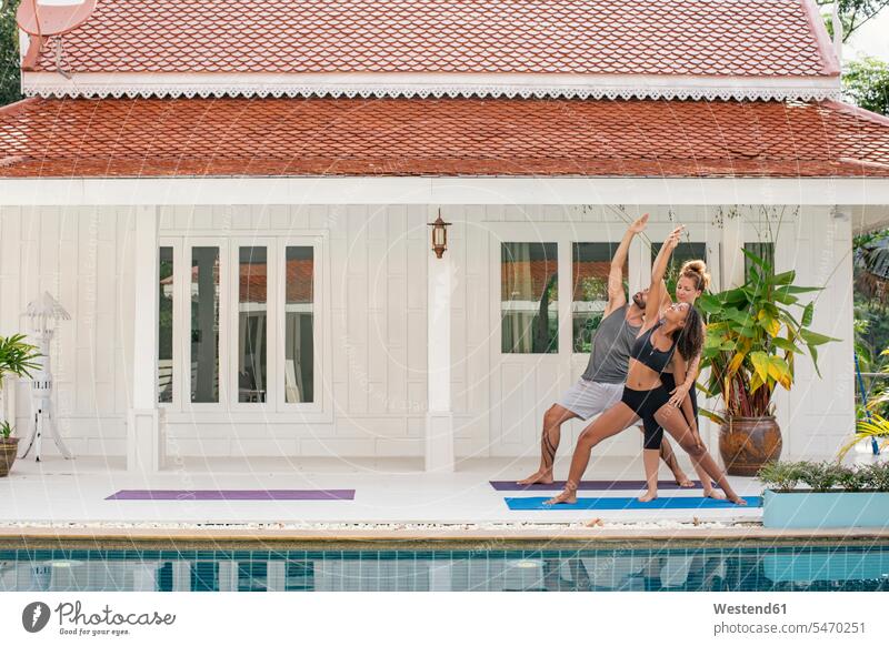 Yogalehrerin unterrichtet Frau in korrekter Yogastellung auf der Terrasse Yogaposition Yogaübung Asana korrigieren korrigiert Swimmingpool Swimmingpools