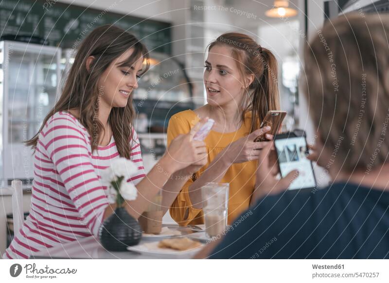 Zwei Freundinnen treffen sich mit Hilfe von Smartphones in einem Café sitzen sitzend sitzt Treffen Begegnung Cafe Kaffeehaus Bistro Cafes Kaffeehäuser Freunde