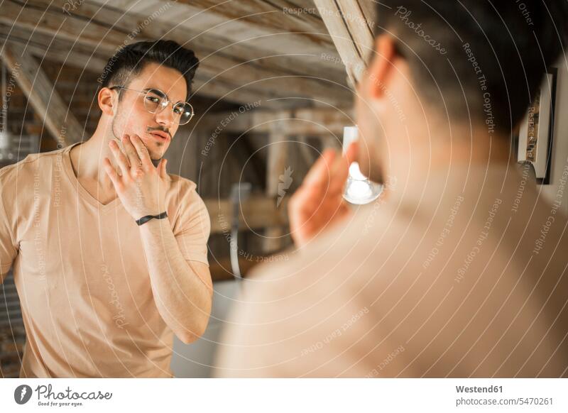 Junger Mann schaut in den Badezimmerspiegel Spiegel schauen schauend anschauen betrachten Männer männlich Zimmer Raum Räume sehend Erwachsener erwachsen Mensch