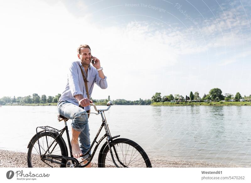Erwachsener Mann mit Fahrrad mit Smartphone am Rheinufer Bikes Fahrräder Räder Rad benutzen benützen Radfahrer Fahrradfahrer iPhone Smartphones Anruf