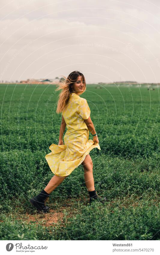 Junge Frau zu Fuß in einem grünen Feld Blickkontakt Augenkontakt Sommer Sommerzeit sommerlich weiblich Frauen Kleid Kleider lächeln Felder gehen gehend geht