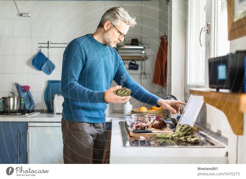 Reifer Mann bereitet Salat in seiner Küche mit digitalem Tablett zu Leute Menschen People Person Personen Europäisch Kaukasier kaukasisch 1 Ein ein Mensch