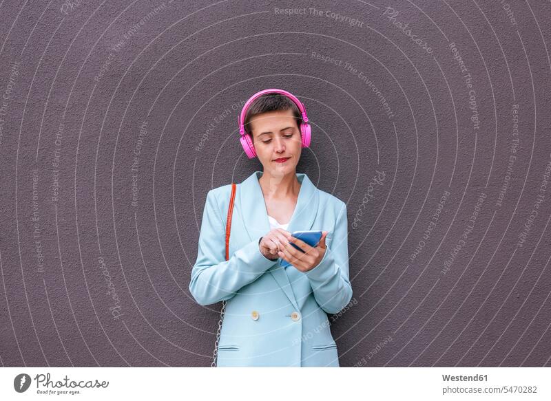 Frau in Jacke, die mit ihrem Handy Musik hört Jackett Anzugjacke Smartphone iPhone Smartphones Kopfhörer Kopfhoerer weiblich Frauen hören hoeren Jacken