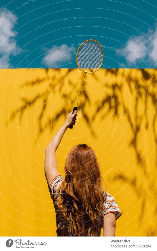 Frau hält Badmintonschläger über gelbe Wand an sonnigem Tag Farbaufnahme Farbe Farbfoto Farbphoto Außenaufnahme außen draußen im Freien Tageslichtaufnahme