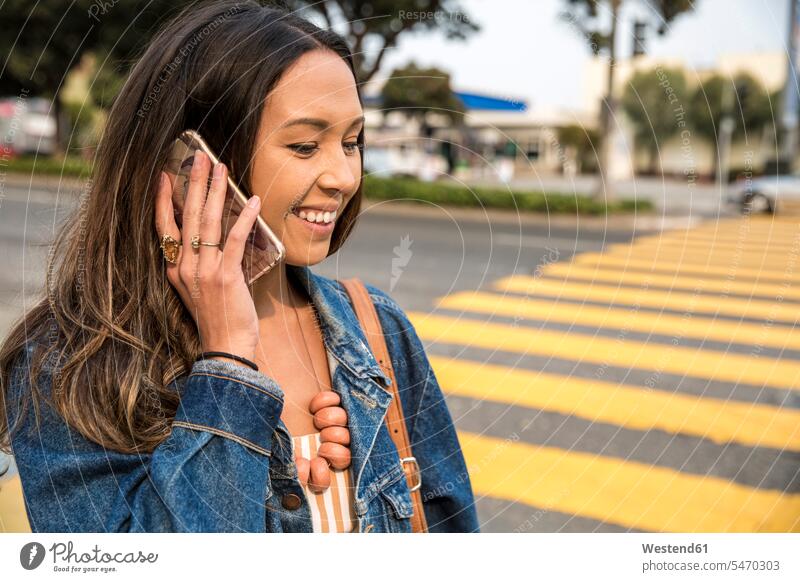 Lächelnde junge Frau redet auf der Straße mit einem Smartphone lächeln iPhone Smartphones telefonieren anrufen Anruf telephonieren Strassen Straßen weiblich