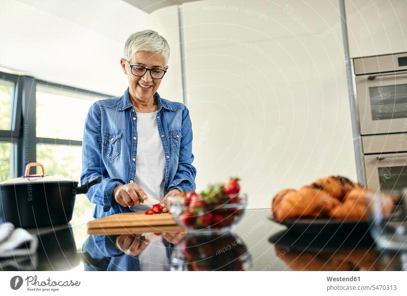 Ältere Frau steht in der Küche und hackt Erdbeeren Leute Menschen People Person Personen Europäisch Kaukasier kaukasisch erwachsen Erwachsene Frauen weiblich