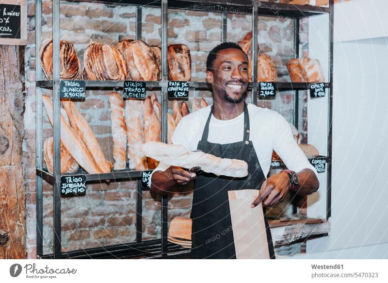 Lächelnder Mann bei der Arbeit in einer Bäckerei Job Berufe Berufstätigkeit Beschäftigung Jobs handeln Verkaeufer Schilder Zeichen Ablage Regale Kauf freuen