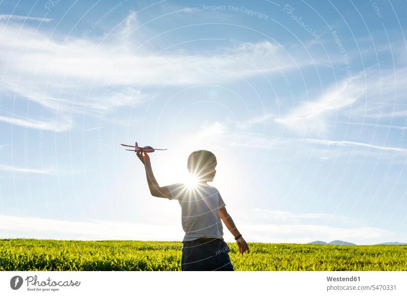 Verspielter Junge hält Flugzeugspielzeug, während er gegen den klaren Himmel steht Farbaufnahme Farbe Farbfoto Farbphoto Außenaufnahme außen draußen im Freien