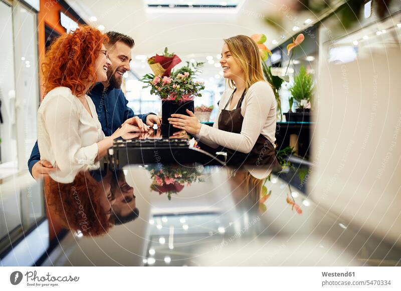 Glückliches Paar und Verkäuferin mit Topfpflanze am Tresen im Blumenladen Kunde Kunden Kundschaft Blumengeschäft Blumengeschaeft Blumenläden Blumenlaeden