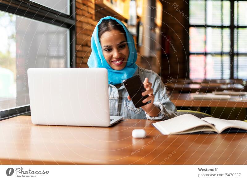 Geschäftsfrau mit türkisfarbenem Hijab in einem Café, die mit Laptop und Smartphone arbeitet Job Berufe Berufstätigkeit Beschäftigung Jobs geschäftlich