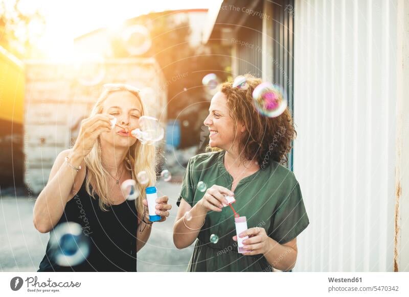 Zwei glückliche Frauen blasen Seifenblasen im Freien weiblich Freundinnen Spaß Spass Späße spassig Spässe spaßig Glück glücklich sein glücklichsein Erwachsener